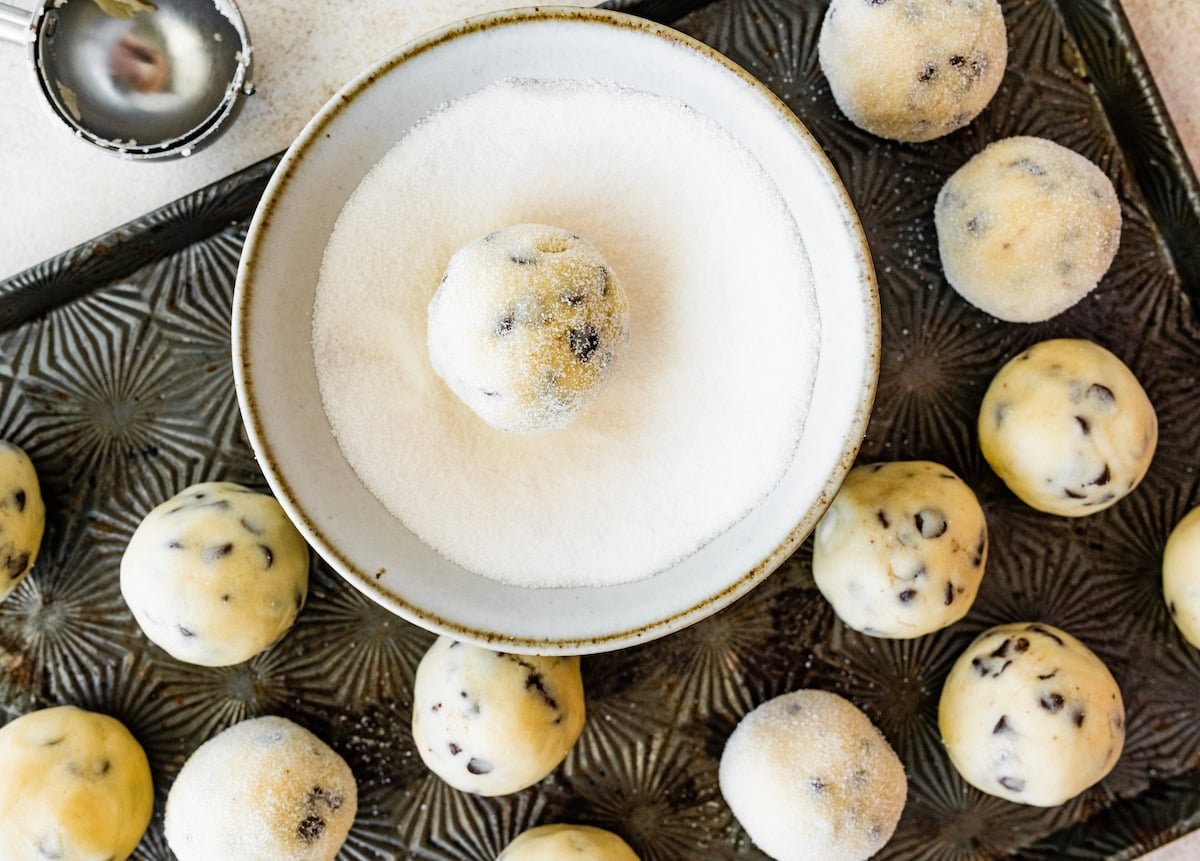 chocolate chip sugar cookie balls being rolled in granulated sugar.