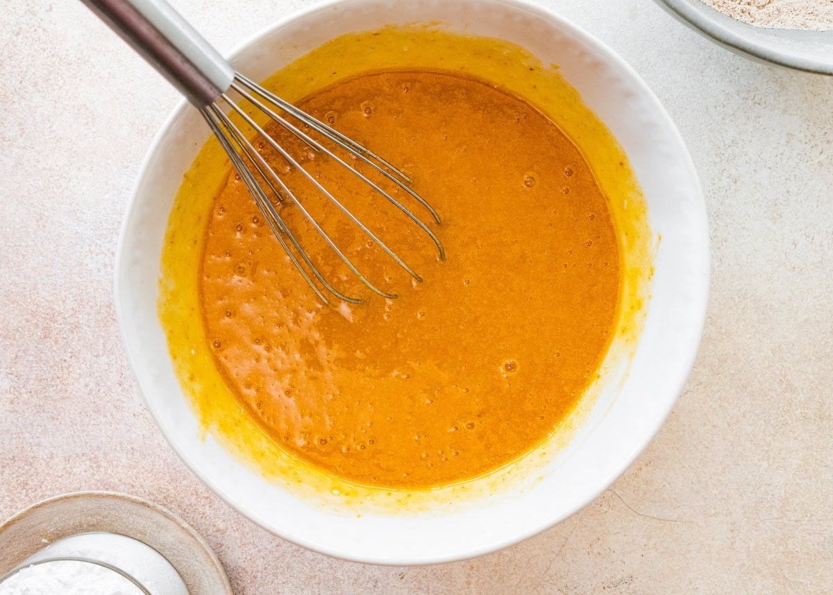 pumpkin roll cake batter in mixing bowl with spatula.