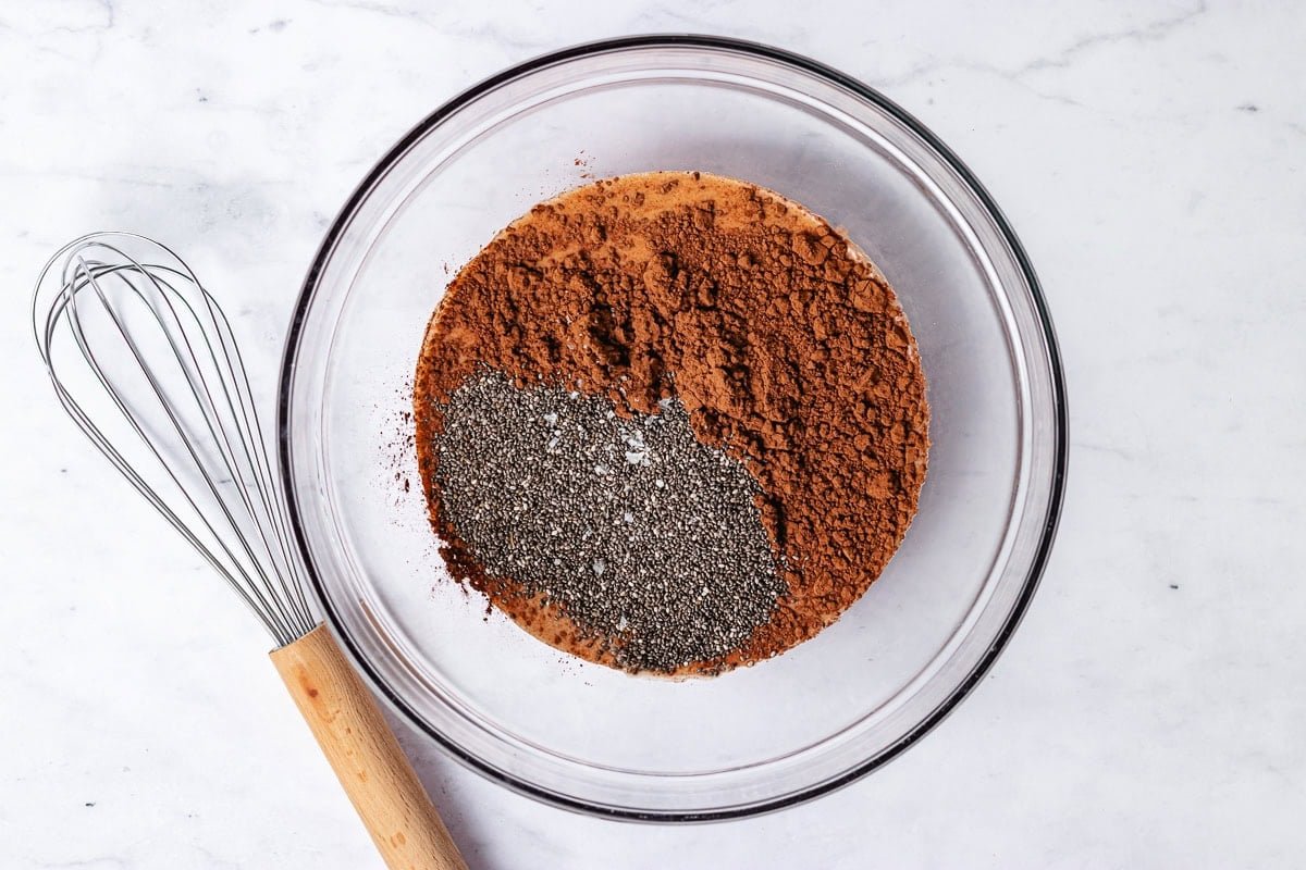 milk, cocoa powder and chia seeds in glass mixing bowl with whisk to make chocolate chia pudding.
