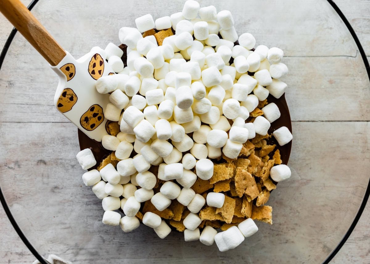 melted chocolate, mini marshmallows, and graham cracker pieces in mixing bowl with spatula.