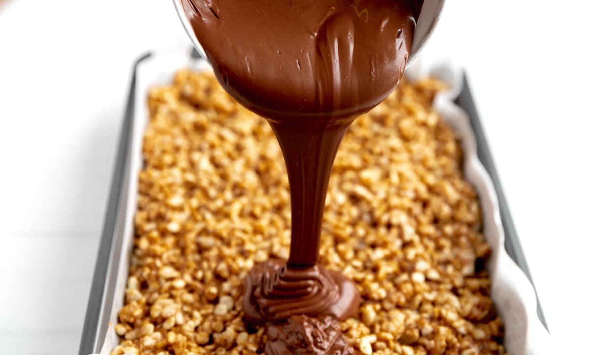 chocolate being poured over scotcheroos in pan.
