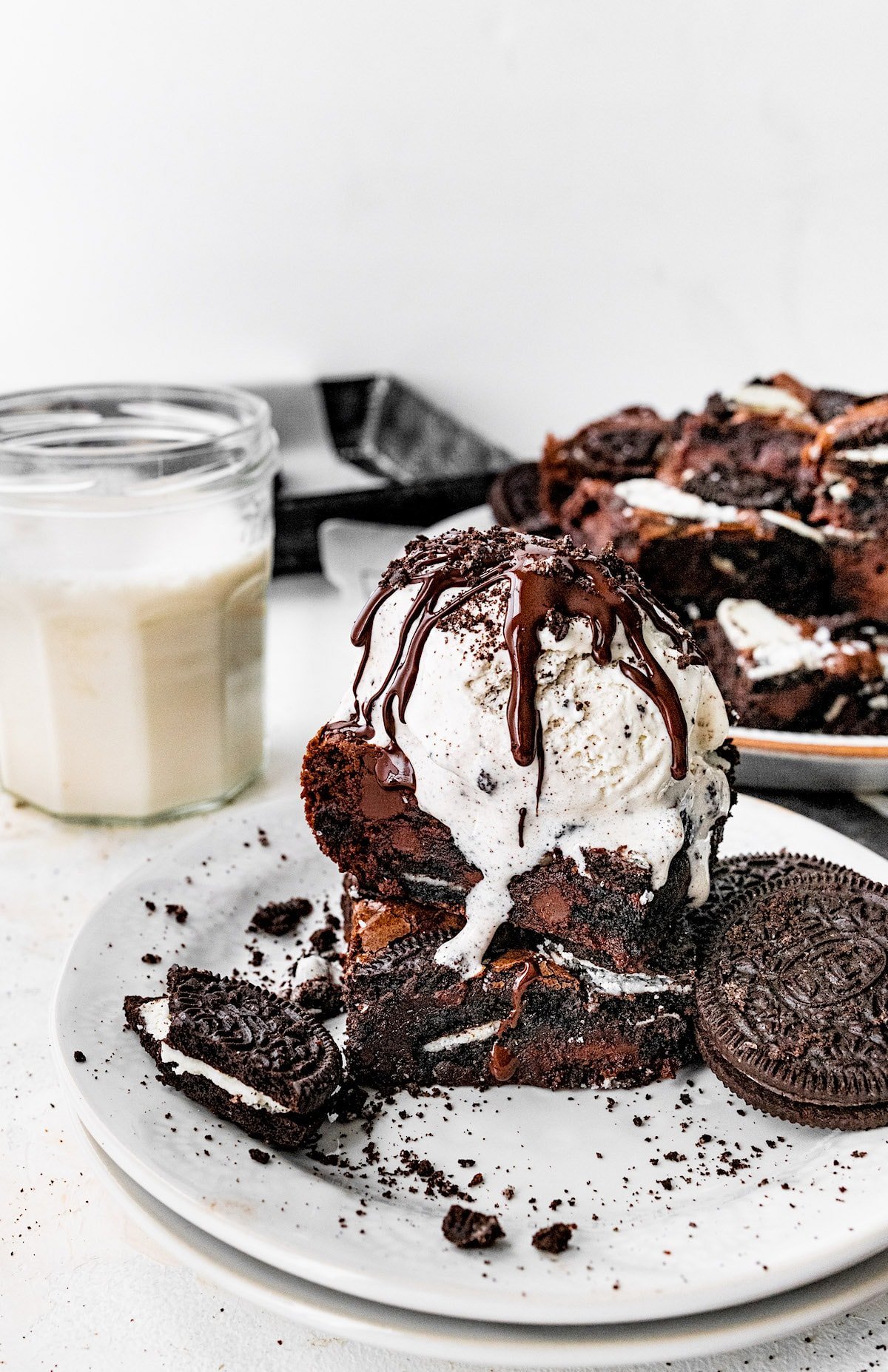 Oreo brownies stacked with cookies and cream ice cream, hot fudge, and Oreos on plate.