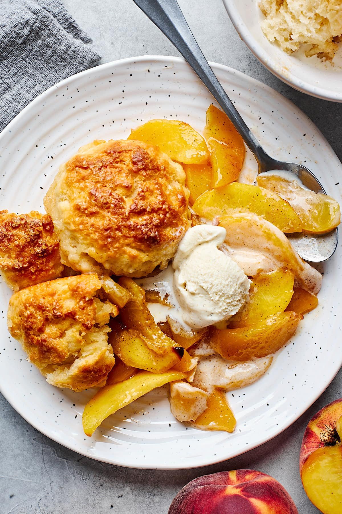 peach cobbler with vanilla ice cream in bowl with spoon.