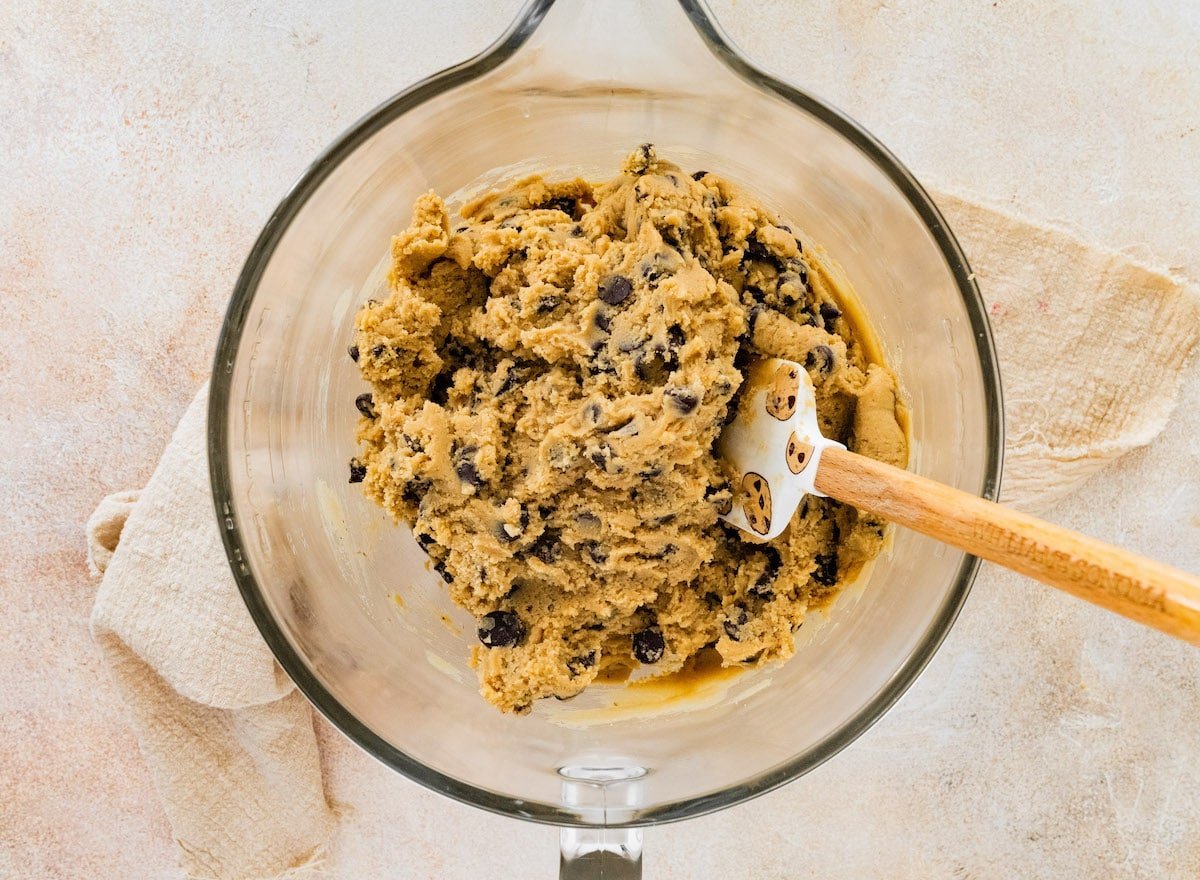 chocolate chip cookie dough in glass mixing bowl with spatula.