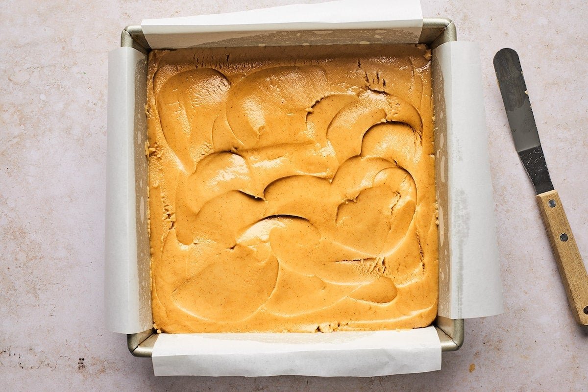 peanut butter fudge pressed in pan with parchment paper.