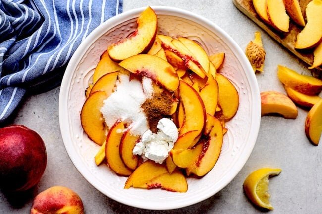 peach slices in bowl with sugar, cinnamon, and cornstarch.