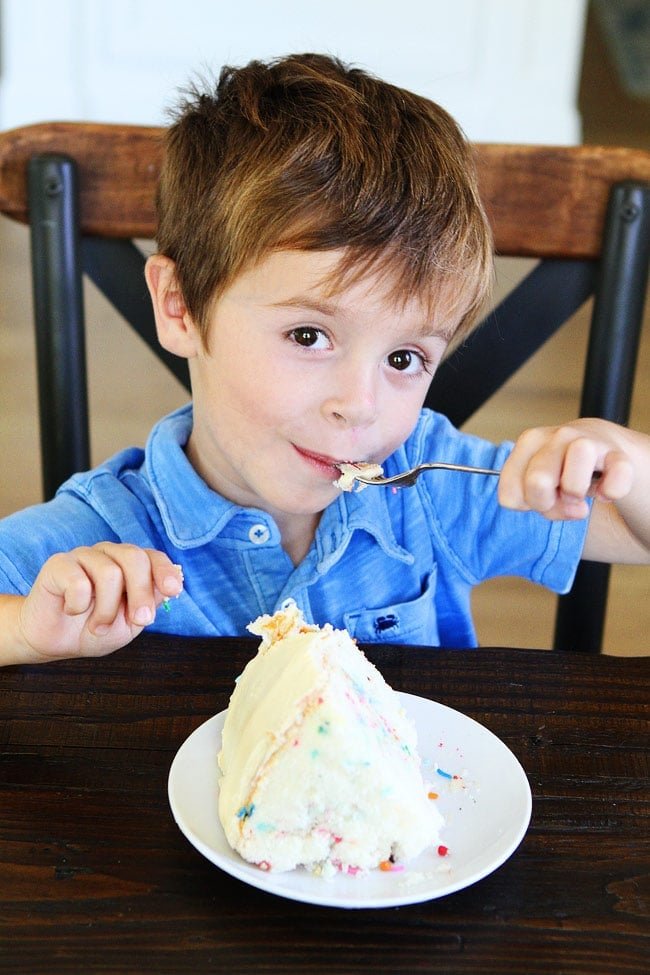 Funfetti Cake Recipe on twopeasandtheirpod.com White layer cake with sprinkles and a sweet vanilla buttercream frosting. This is the perfect party cake! Kid Eating Funfetti Cake