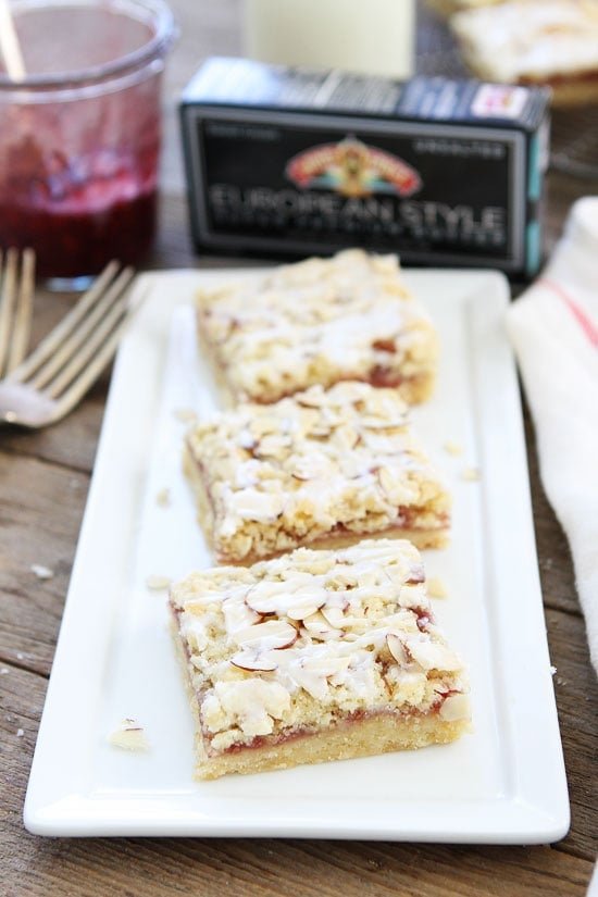 Raspberry Almond Shortbread Bars Recipe on twopeasandtheirpod.com Buttery shortbread bars with raspberry jam, almond streusel, and a sweet almond glaze! Dessert perfection! Raspberry Almond Shortbread Bars Recipe