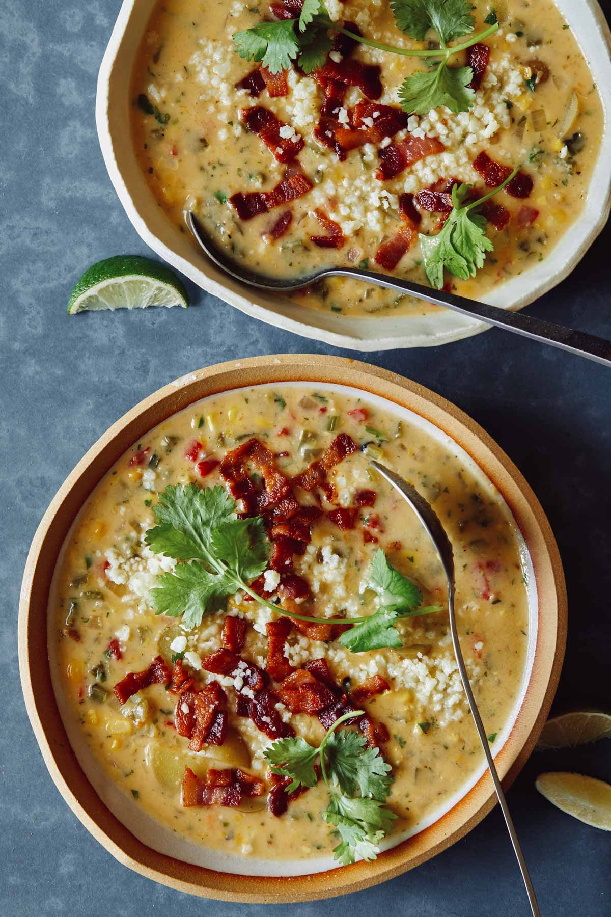 Two bowls of chowder overhead with some lime wedges on the side and spoons.