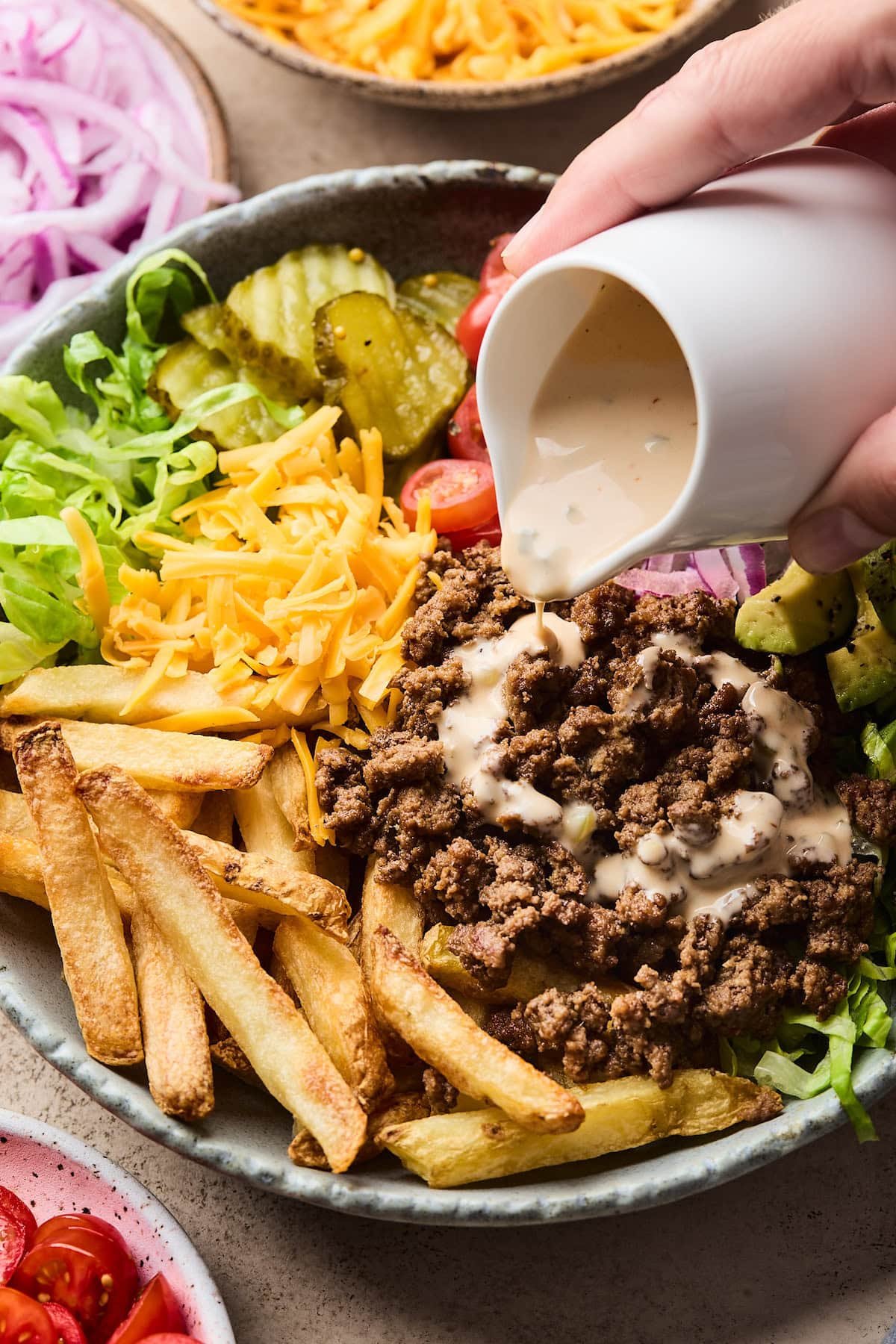 special sauce being poured over burger bowl.