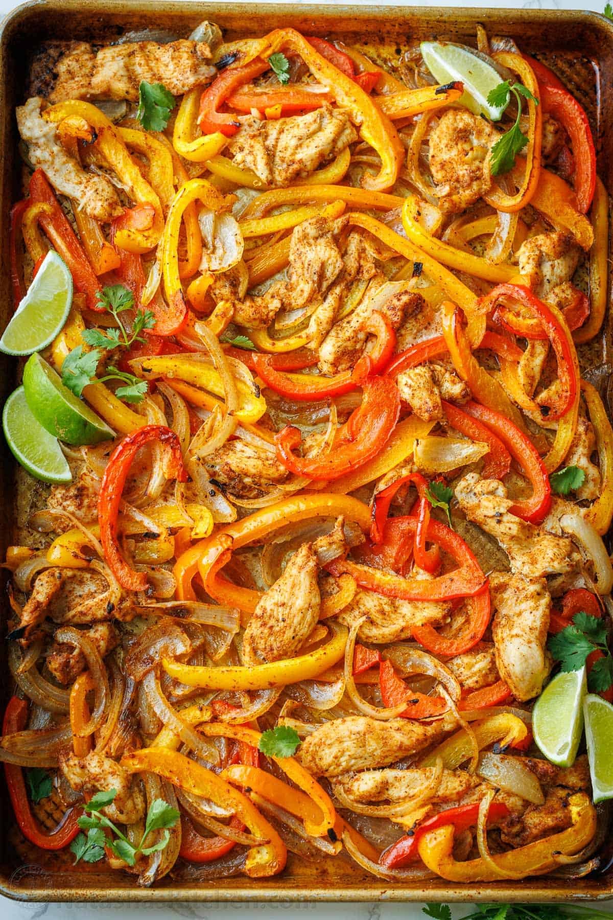 Sheet Pan Chicken Fajitas recipe packed with flavor. It's a crowd-pleasing, 30-minute, one pan meal that makes any weeknight meal a fiesta! Sheet Pan Fajitas spread onto a cookie sheet with lime wedges and cilantro