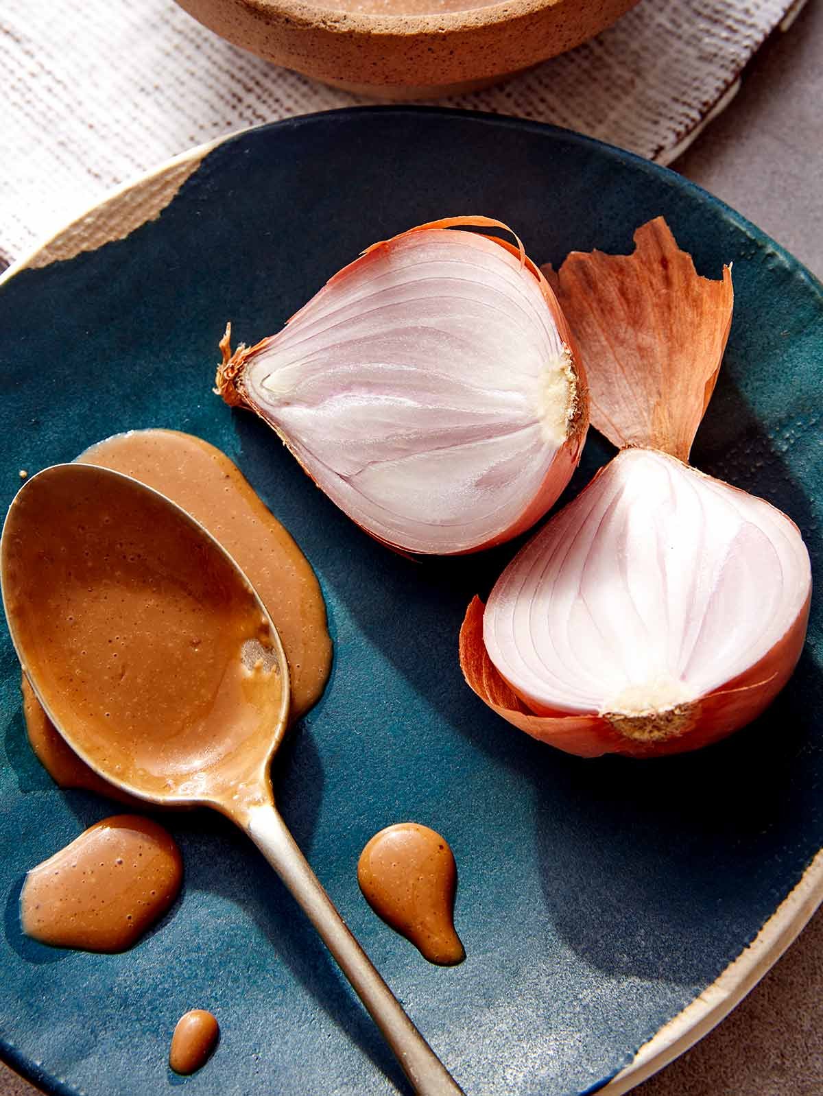 A spoon with balsamic vinaigrette on it resting on a plate with shallots next to it.