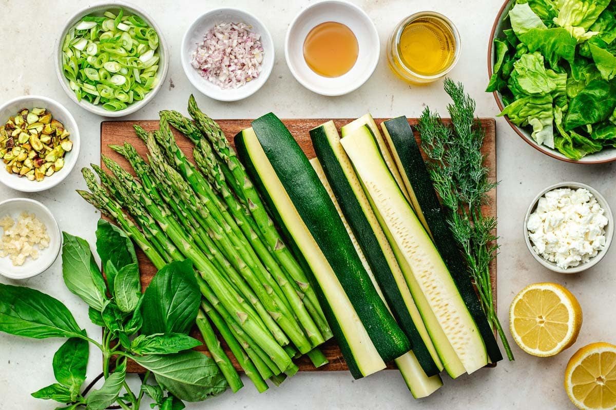 asparagus, zucchini, and herbs on cutting board and ingredients in bowls to make grilled asparagus and zucchini salad.