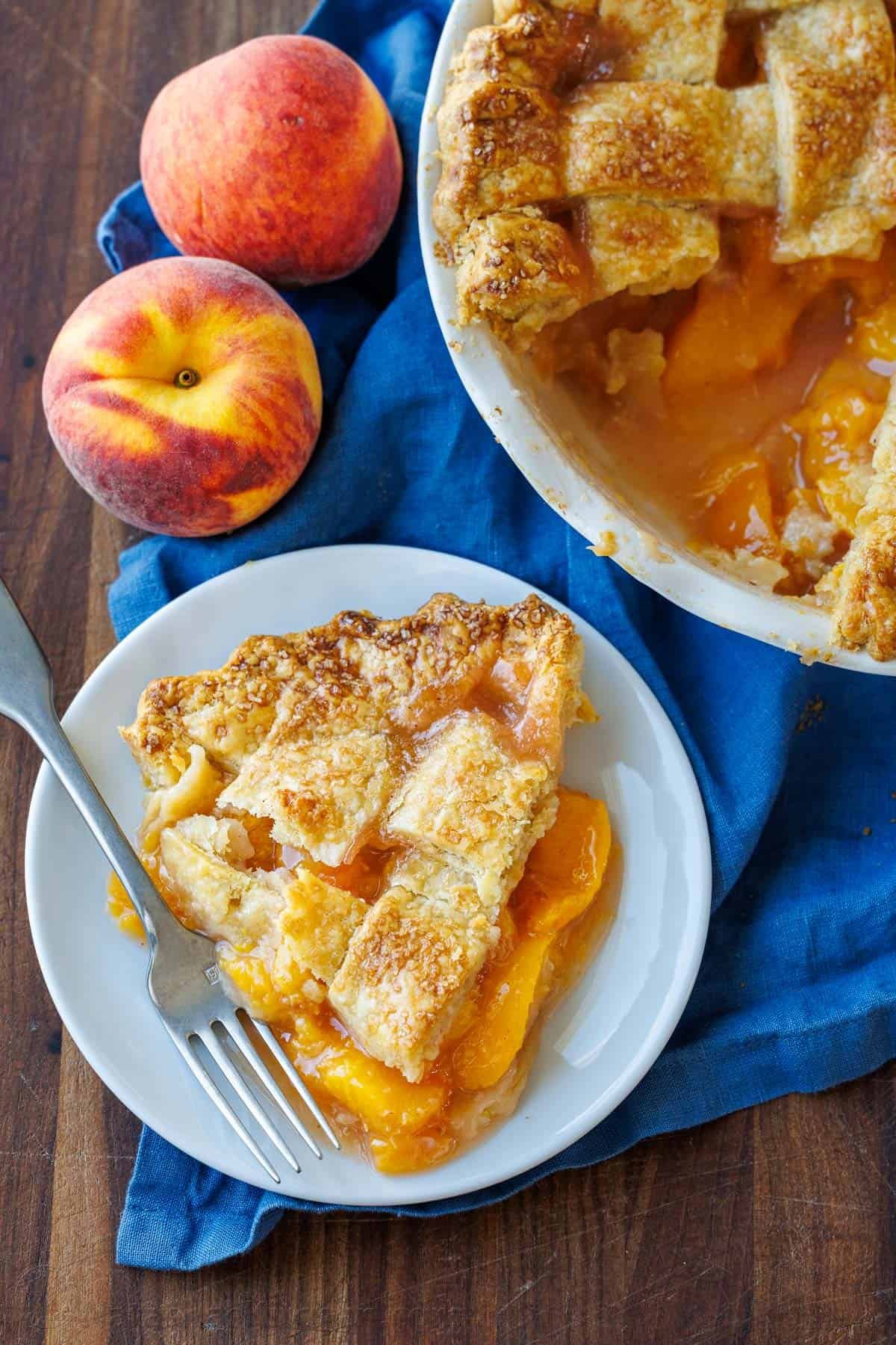 Slice of peach pie on a white plate with pie in the background