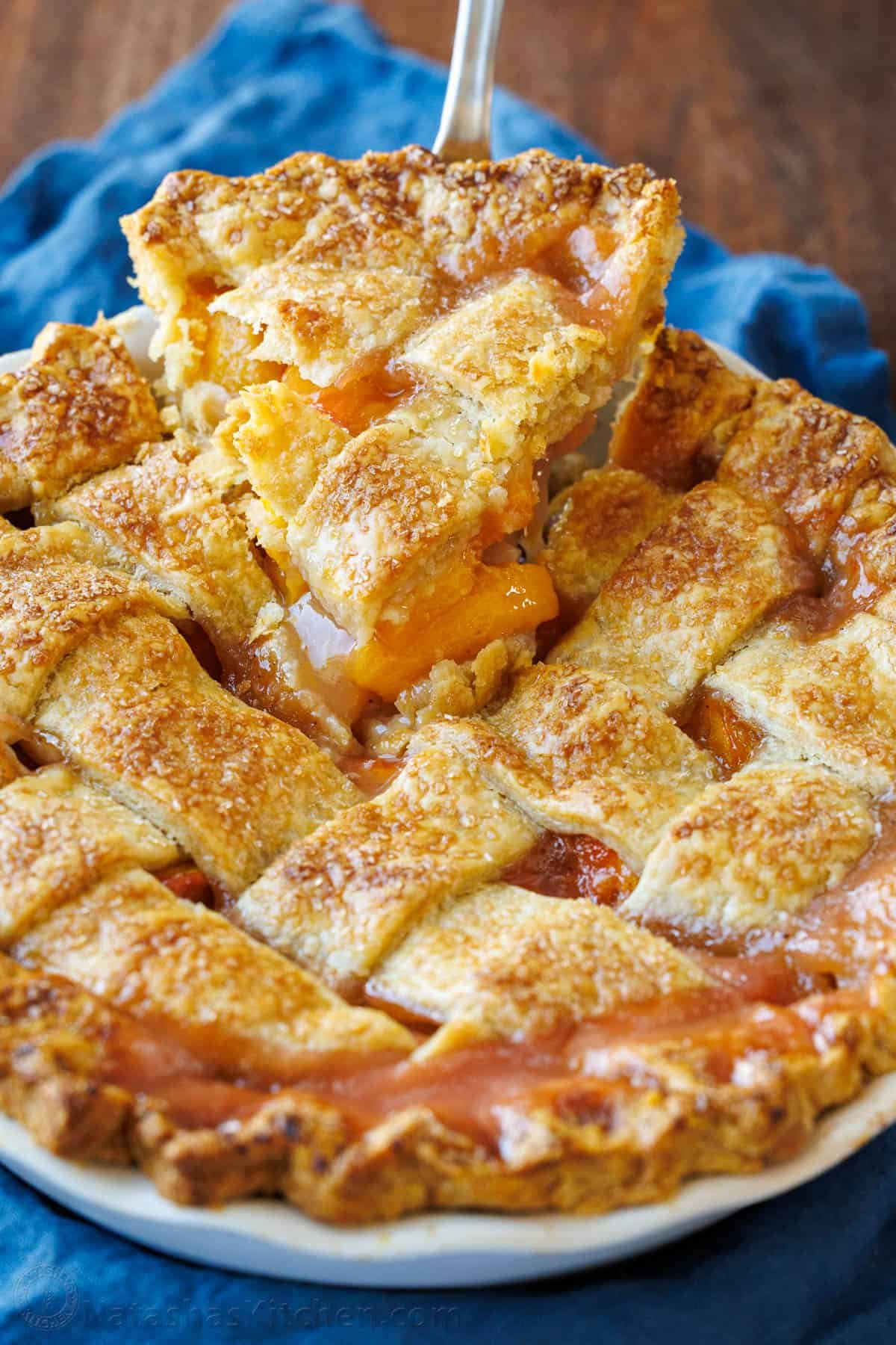 Slice of peach pie lifting out of the dish with blue napkin