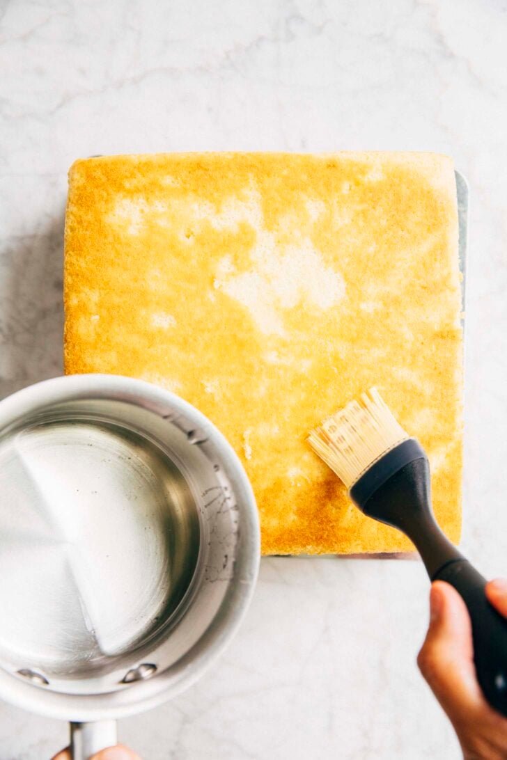 photo of Michelle from Hummingbird High covering the second white almond cake layer with simple syrup