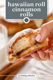 Hand holding up a hawaiian roll cinnamon roll with a bite taken from it. Text overlay includes recipe name.