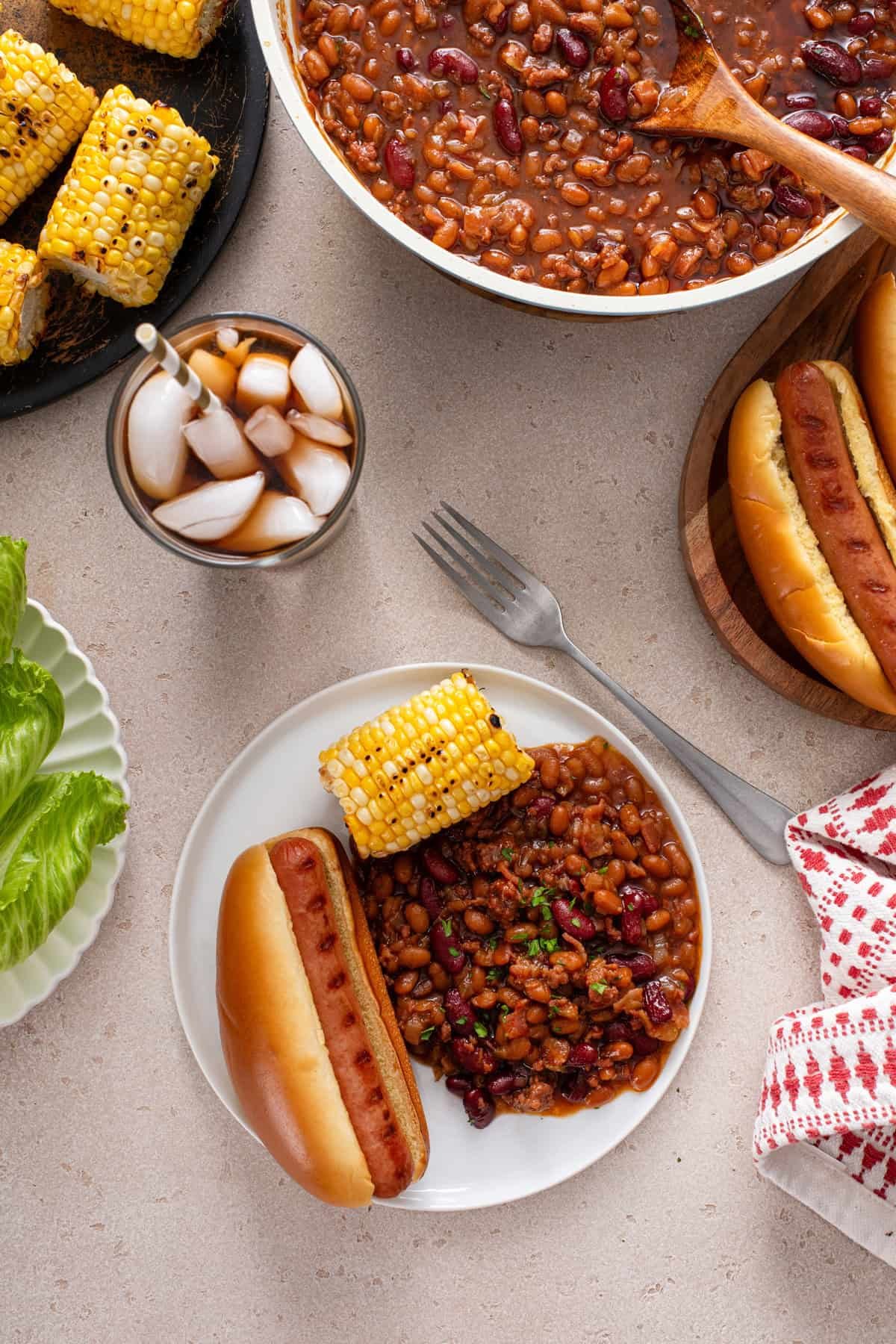 Overhead view of easy baked beans on a white plate with a hot dog and corn.