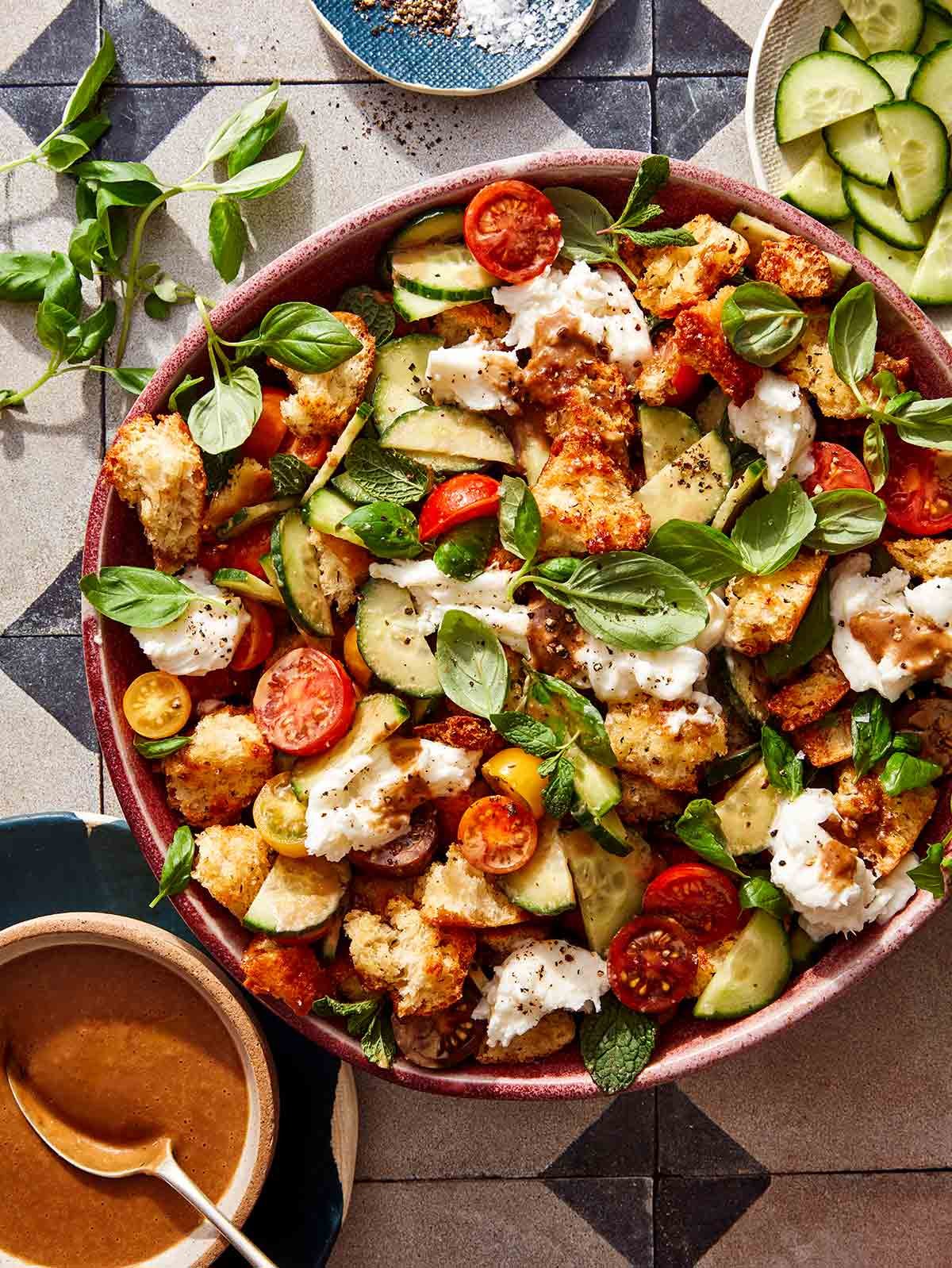 Panzanella salad ready to be served with fresh herbs and ingredients next to it.
