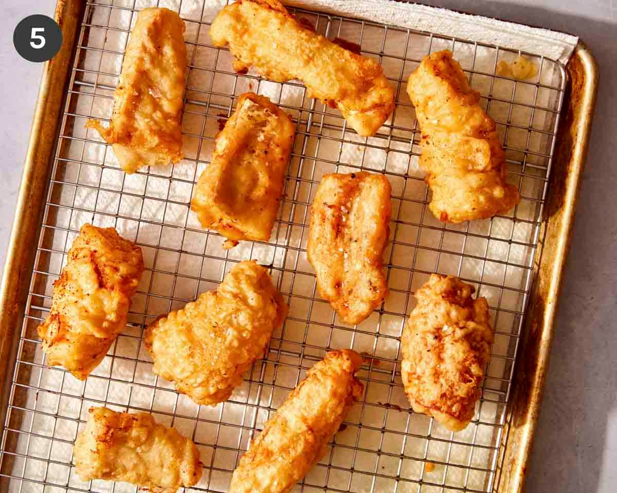 Freshly fried cod fillets on a baking sheet with salt and pepper.