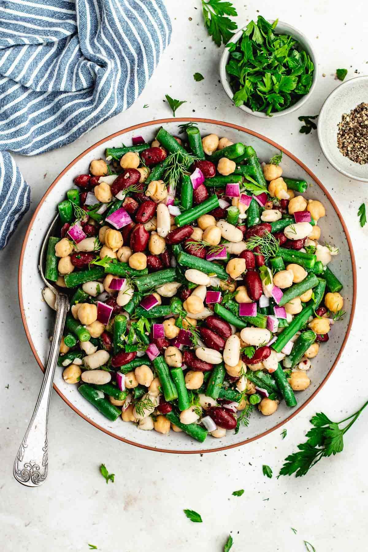 easy bean salad with green beans, chickpeas, white beans, red beans, and herbs in bowl with serving spoon.