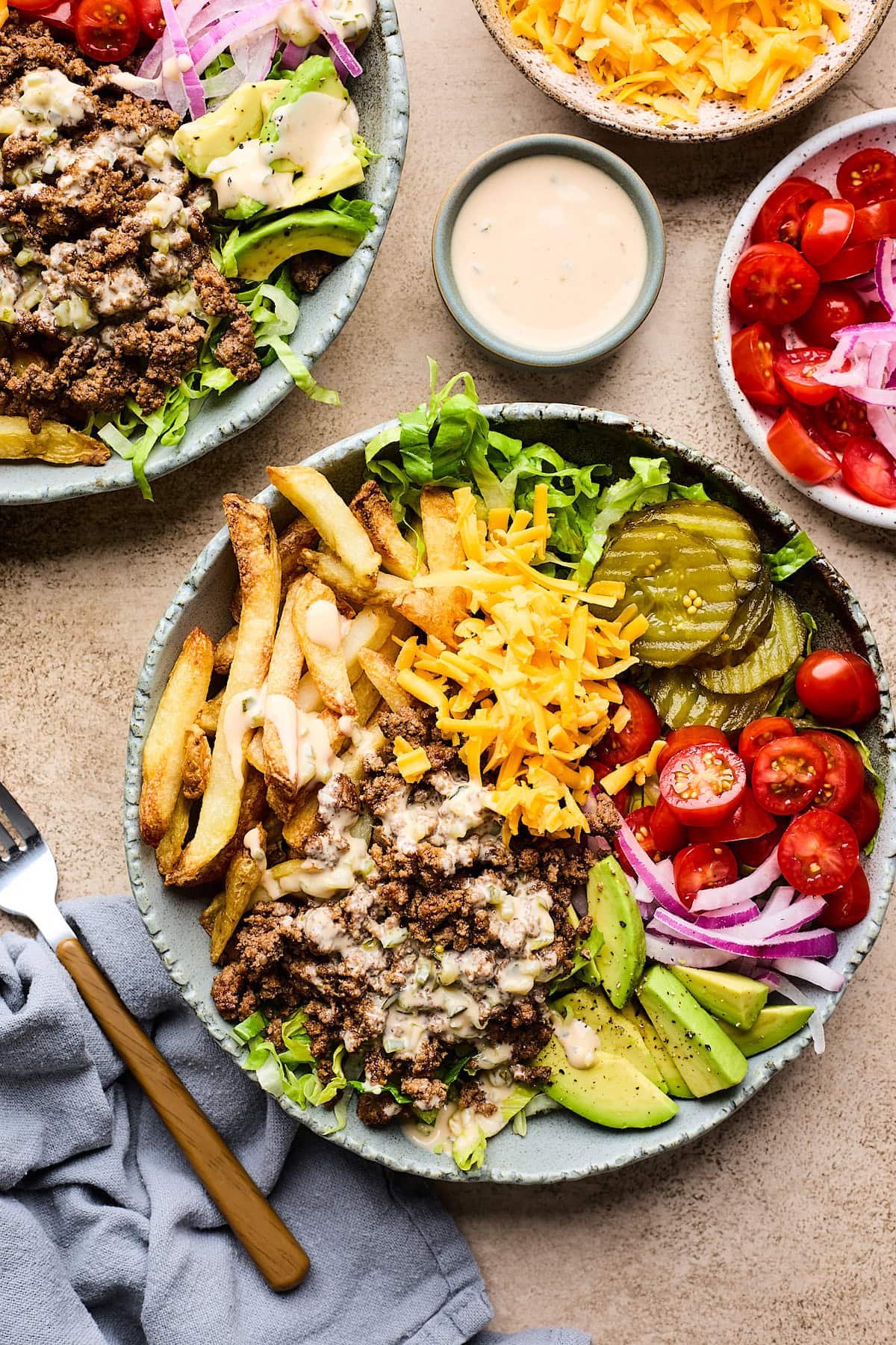 burger bowls with lettuce, fries, cheese, pickles, tomatoes, onion, avocado, and special sauce.
