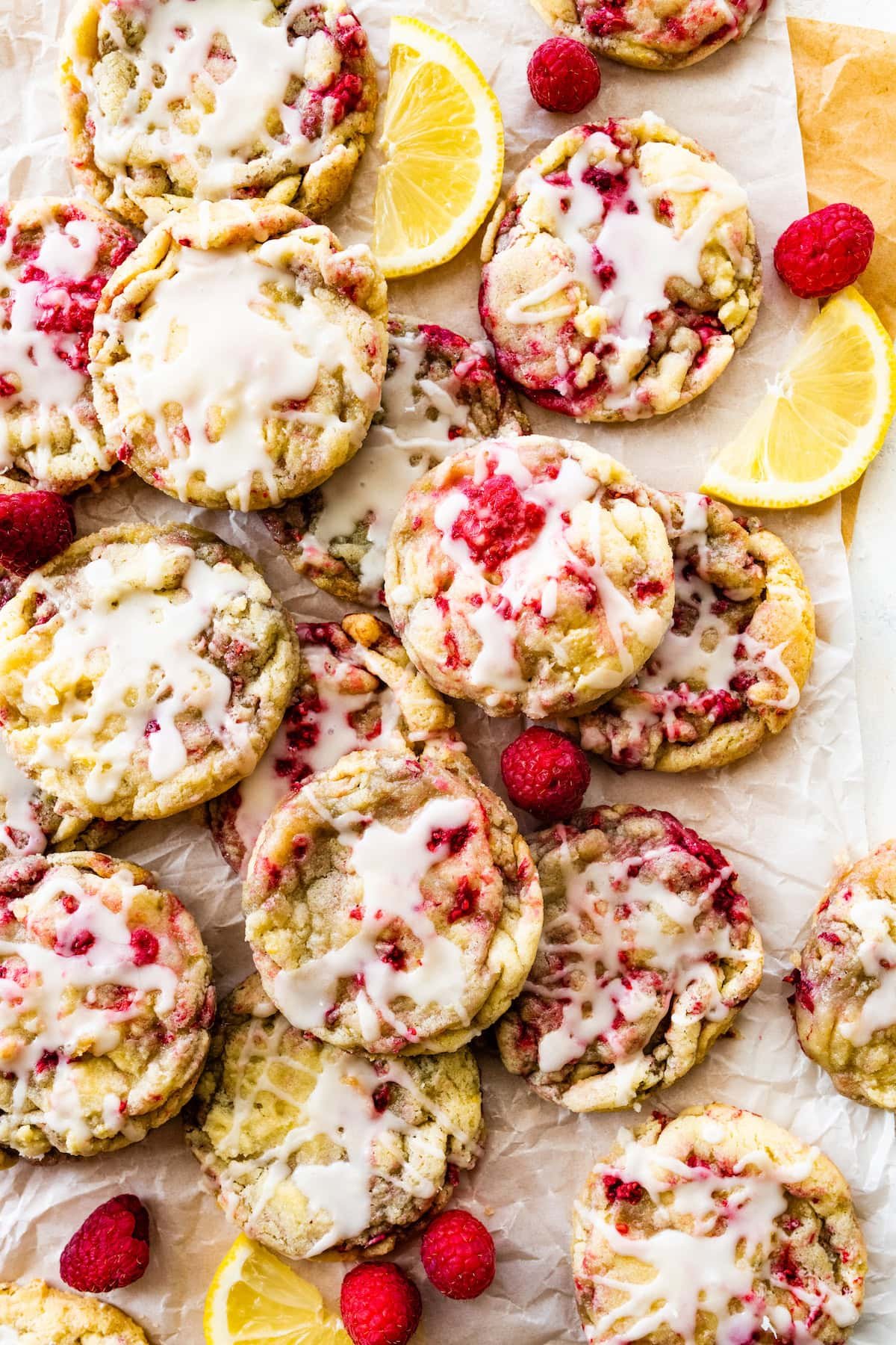 lemon raspberry cookies with lemon glaze on parchment paper with lemon wedges and raspberries.