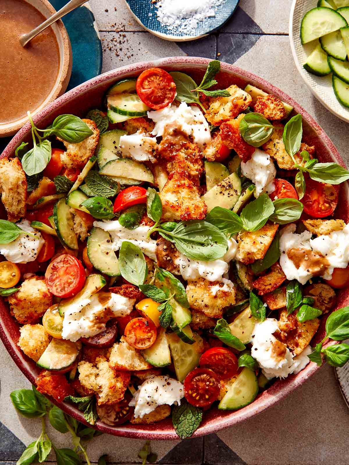 Panzanella salad in a bowl with fresh herbs next to it.