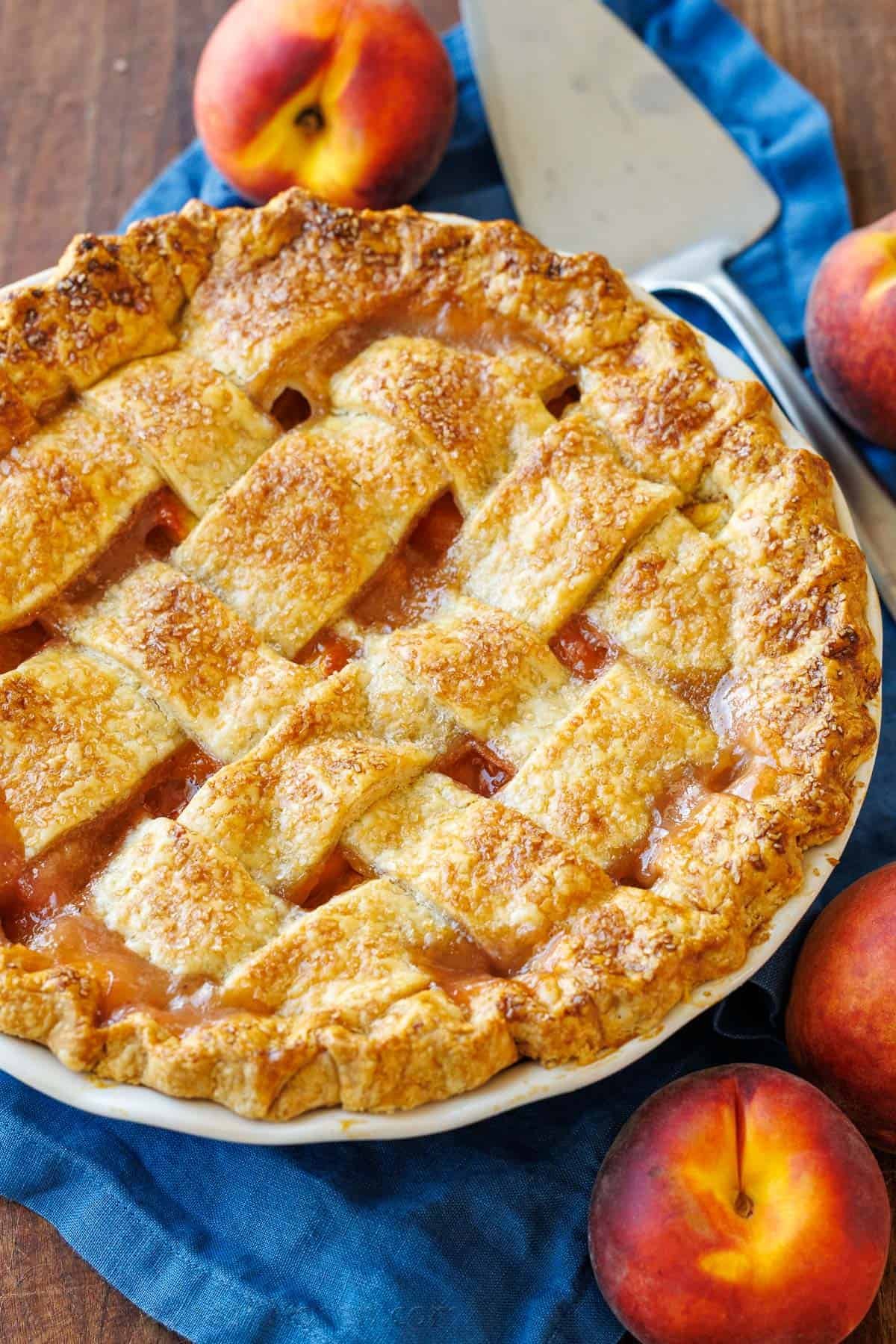 Peaches surrounding a homemade peach pie with browned crust and pie server