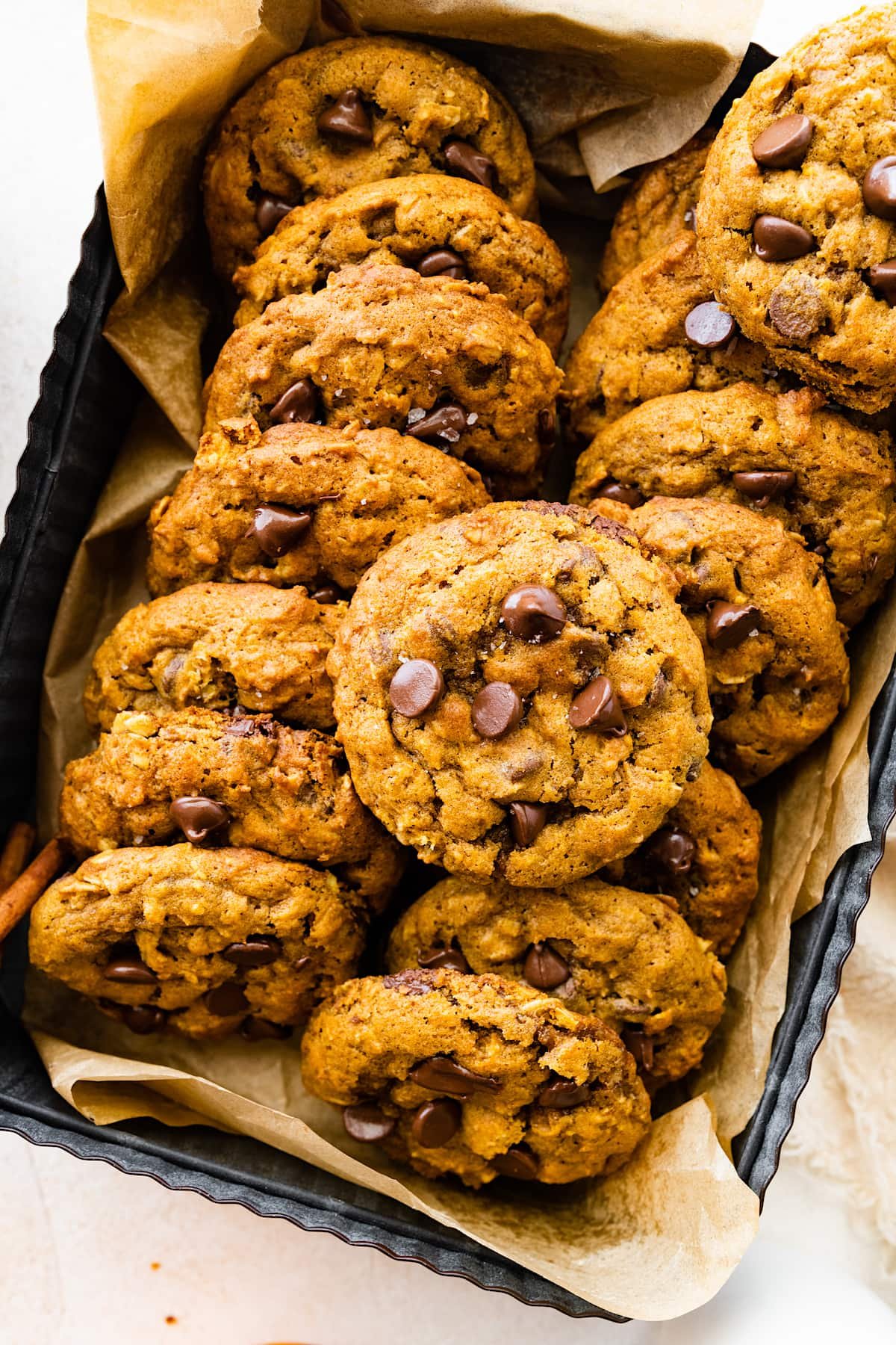 pumpkin oatmeal chocolate chip cookie stacked in pan with parchment paper.