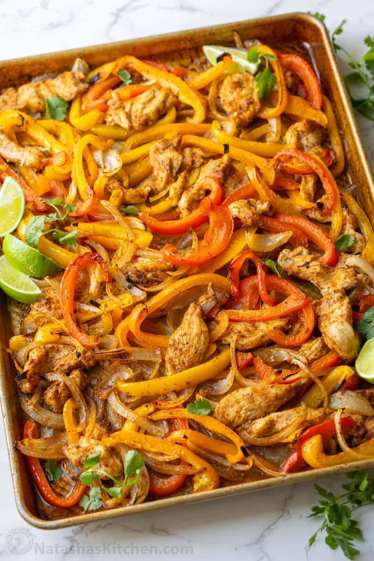 Sheet Pan Chicken Fajitas recipe packed with flavor. It's a crowd-pleasing, 30-minute, one pan meal that makes any weeknight meal a fiesta! sheet pan chicken fajitas cooked on a cookie sheet with chicken, red and yellow peppers, onions and lime wedges