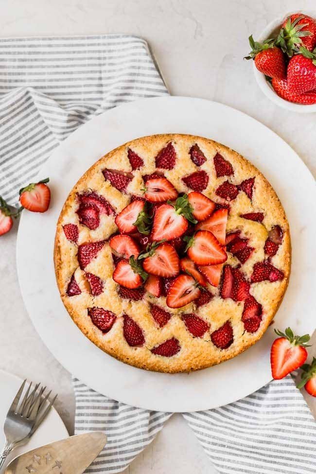 The best homemade strawberry cake recipe and it is SO easy to make! #strawberry #cake #strawberrycake #dessert #spring #vegetarian #easyrecipe homemade strawberry cake with fresh strawberries on top on white round marble board.