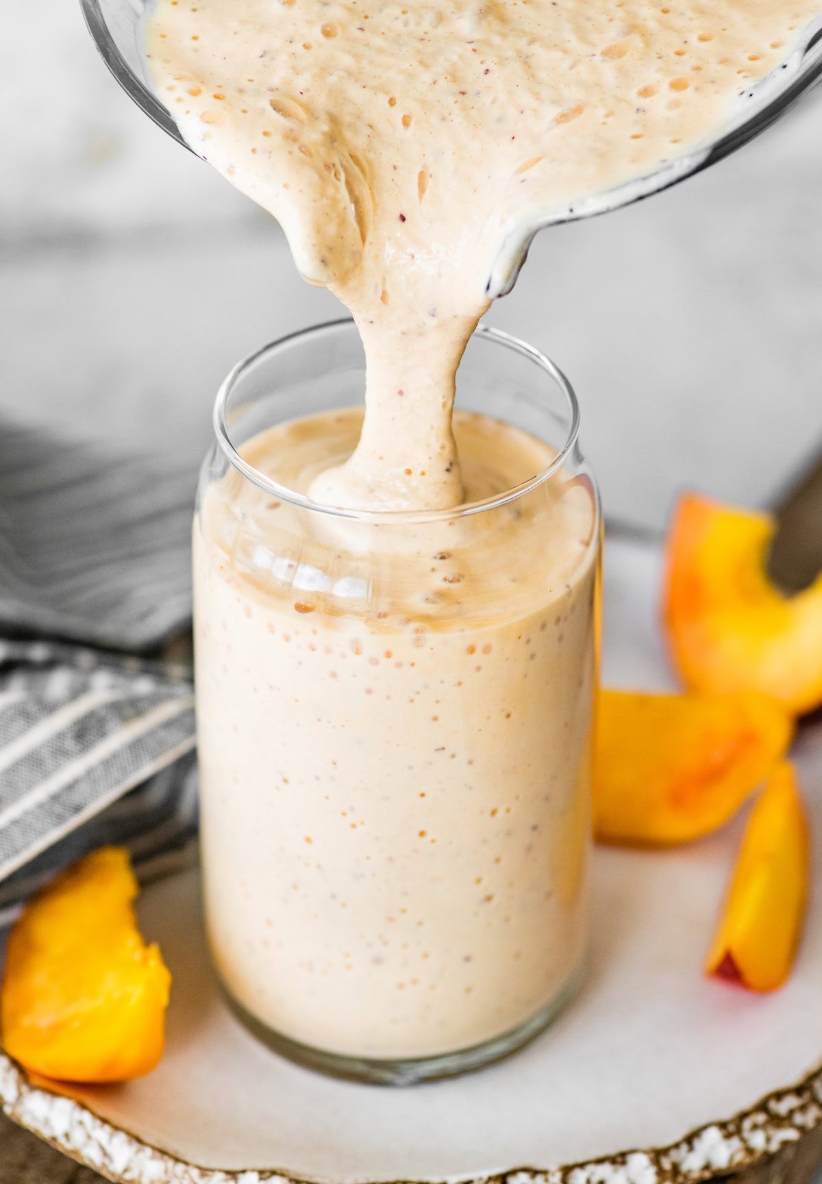 thick peaches and cream smoothie being poured into a glass from the blender. 