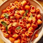 Spicy rigatoni with a tomato sauce in a bowl with basil leaves on top.