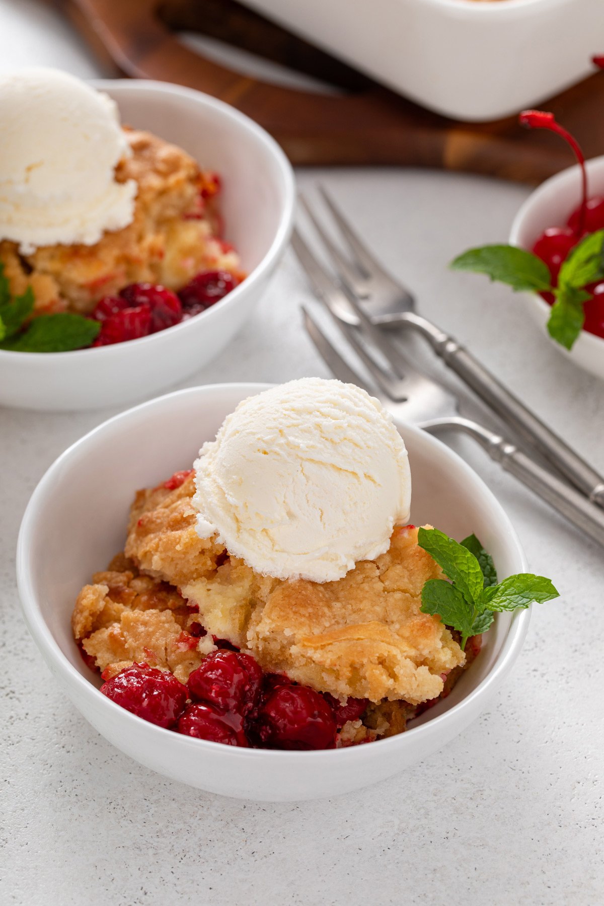 Serving of cherry cheesecake cake topped with ice cream in a white bowl.