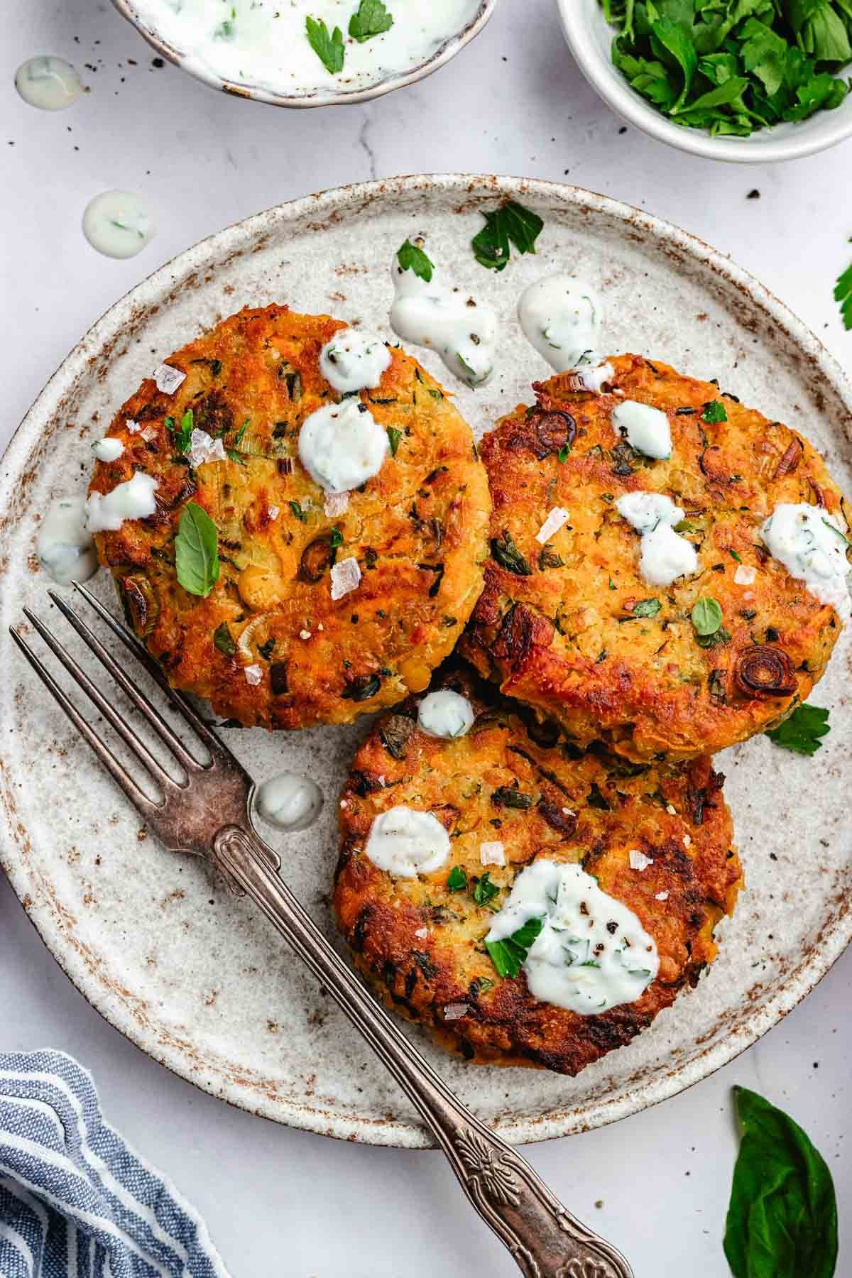 three vegetable chickpea fritters on plate with lemon herb yogurt sauce and fork. 