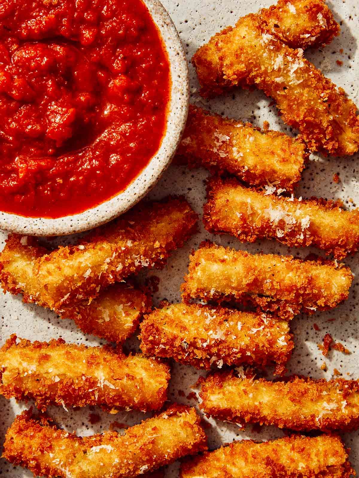 Fried zucchini on a platter and a bowl of marinara next to it.