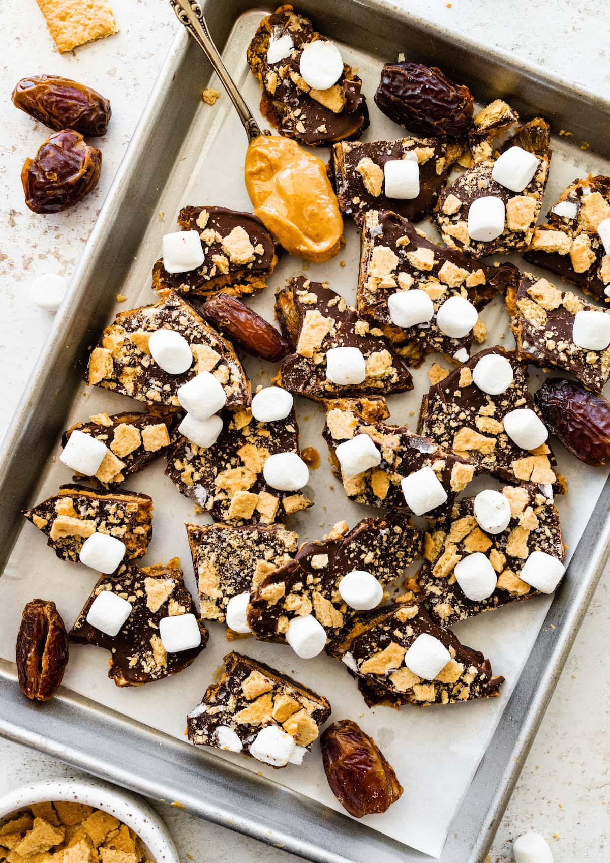 s'mores date bark with peanut butter, graham crackers, and mini marshmallows on sheet pan with parchment paper.