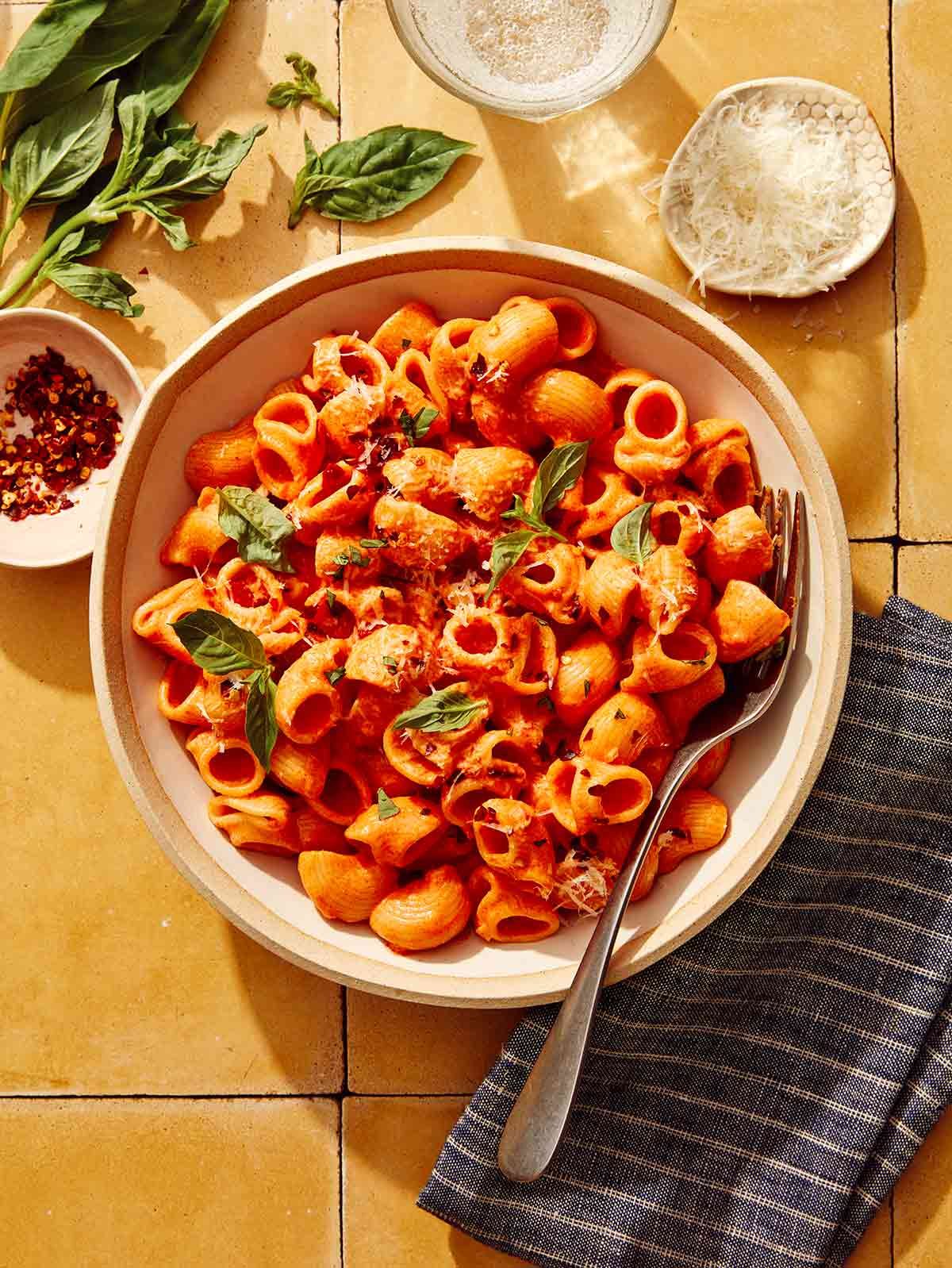 Spicy rigatoni in a bowl with some basil, red pepper flakes, and cheese on the side. 