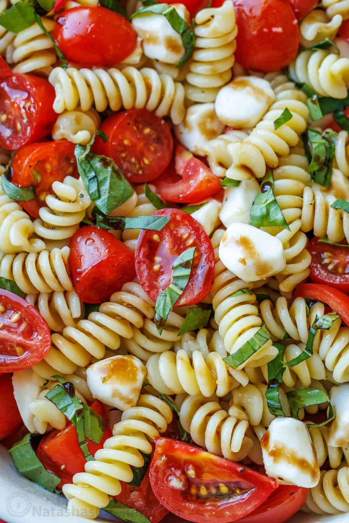 Caprese pasta salad with balsamic glaze and garnished with chopped basil
