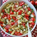 A bowl of Caprese Italian Pasta Salad in a white bowl with balsamic glaze and basil as garnish