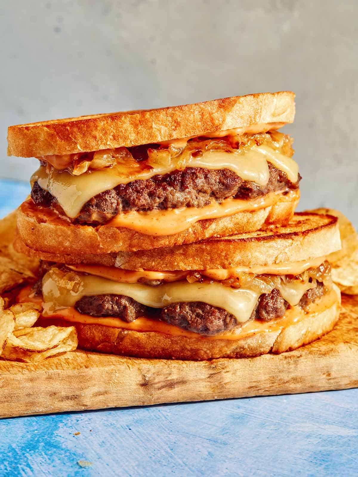 Two patty melt sandwiches on a cutting board.
