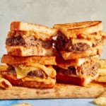 Two patty melts on a cutting board cut in half with chips on the side.