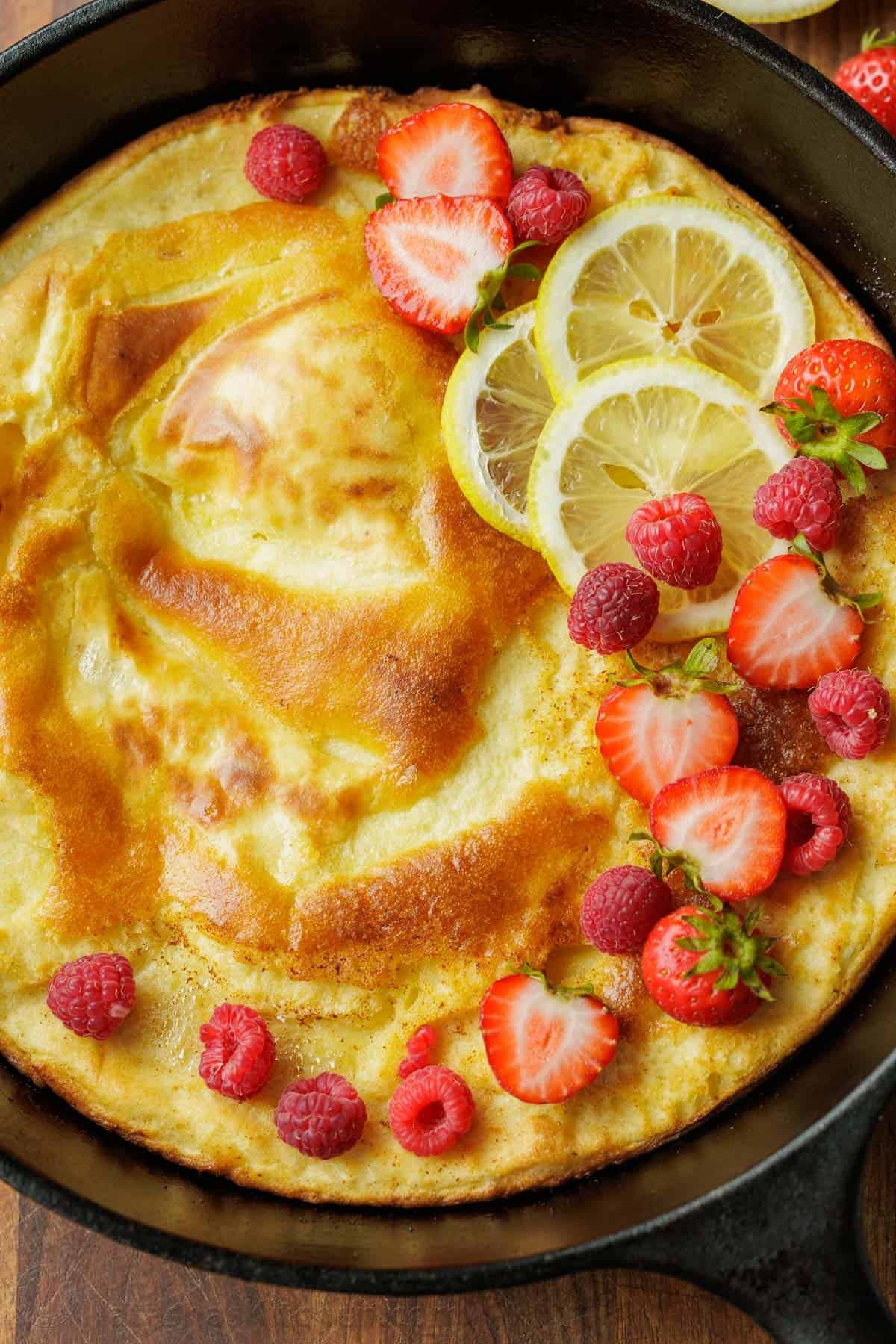 Close up of a German Pancake in a cast iron pan with crispy brown edges and garnished with berries and sliced strawberries