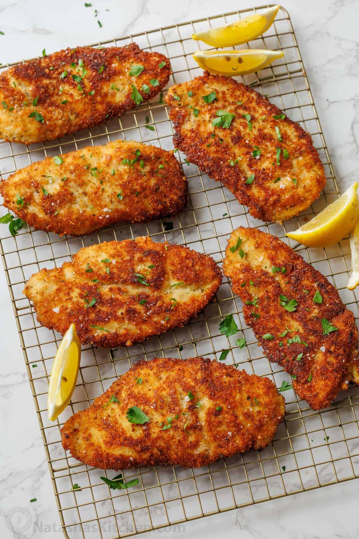 Easy breaded chicken cutlets recipe ready in under 30 minutes. Crispy on the outside with juicy chicken inside. Kid-friendly chicken dinner! Breaded Chicken Cutlets on a wire rack with coarse salt, fresh parsley and lemon slices