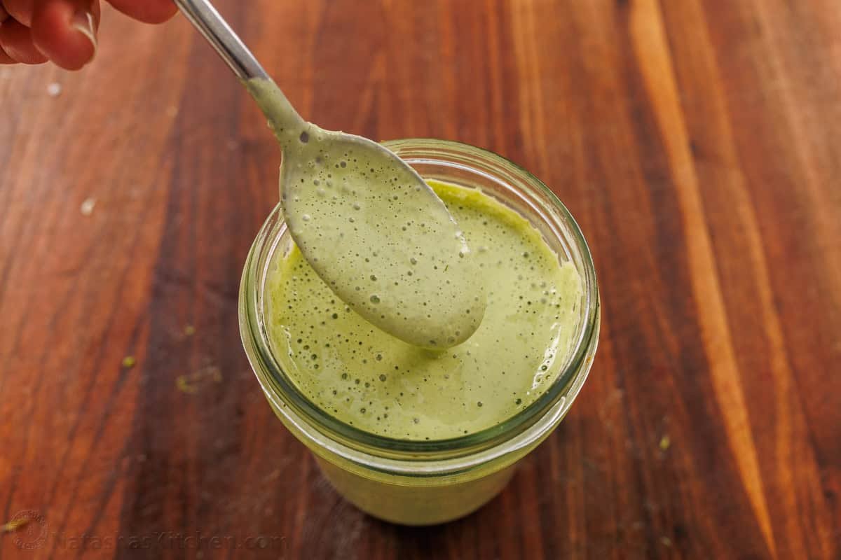 A spoon scooping Green Goddess Dressing out of a mason jar
