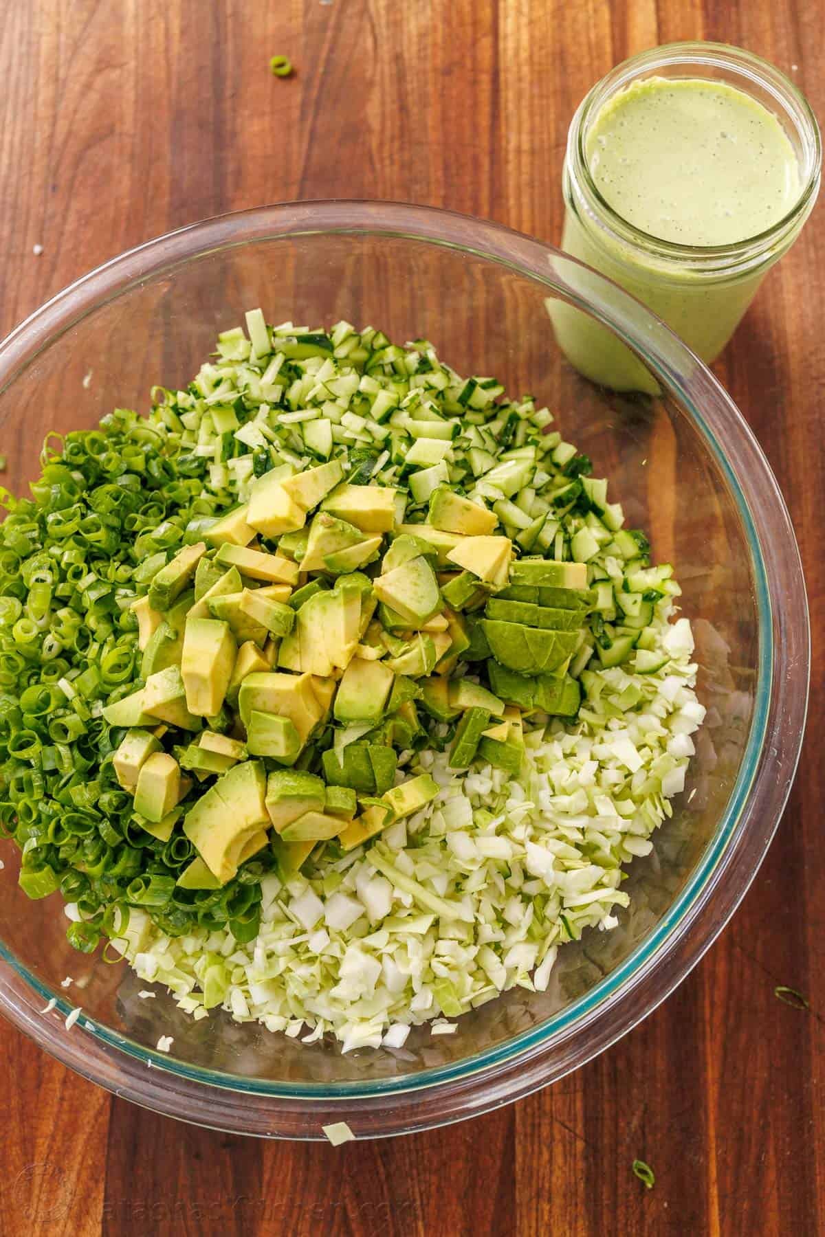 Green Goddess Salad in a bowl with chopped cabbage, cucumbers, avocado, and green onion with Green Goddess dressing in a mason jar on the side