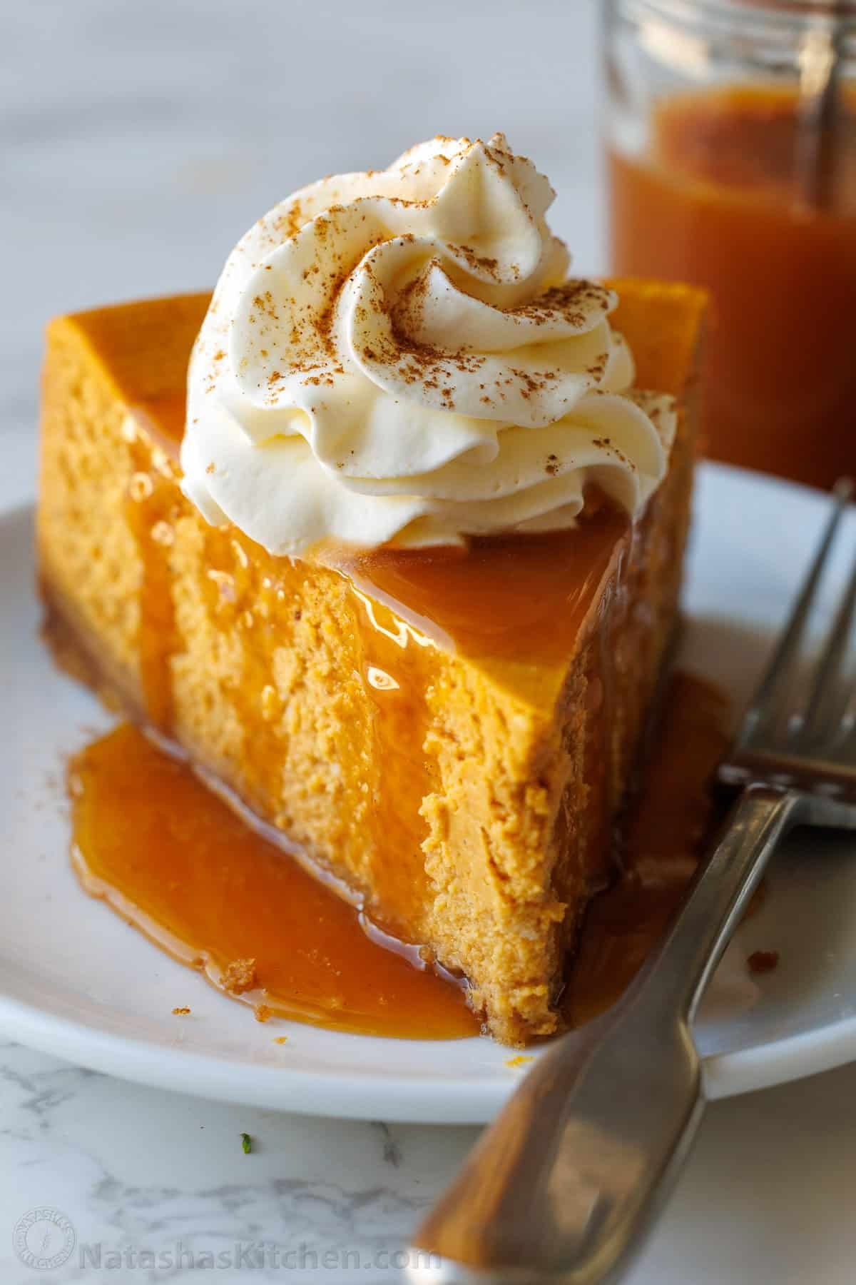 Pumpkin cheesecake garnished with whipped cream and a dusting of cinnamon on a plate with a fork
