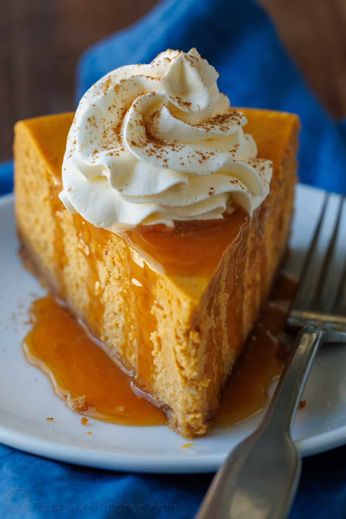 A slice of pumpkin cheesecake with whipped cream on a white plate with a blue napkin.