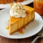 Slice of pumpkin cheesecake on a white plate with caramel drizzle and whipped cream
